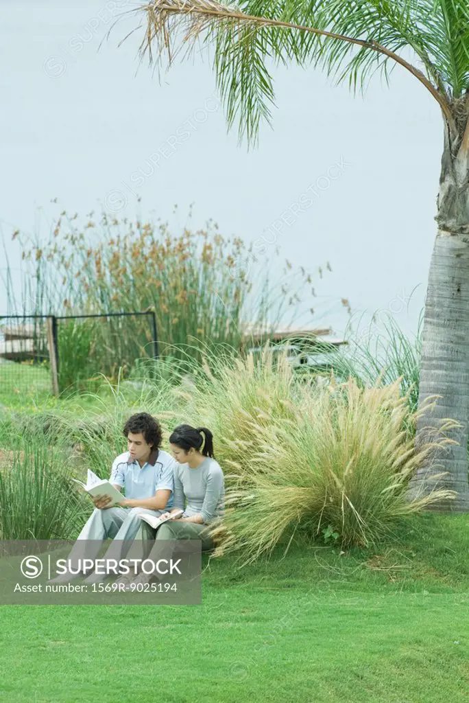 Couple sitting on grass, reading books