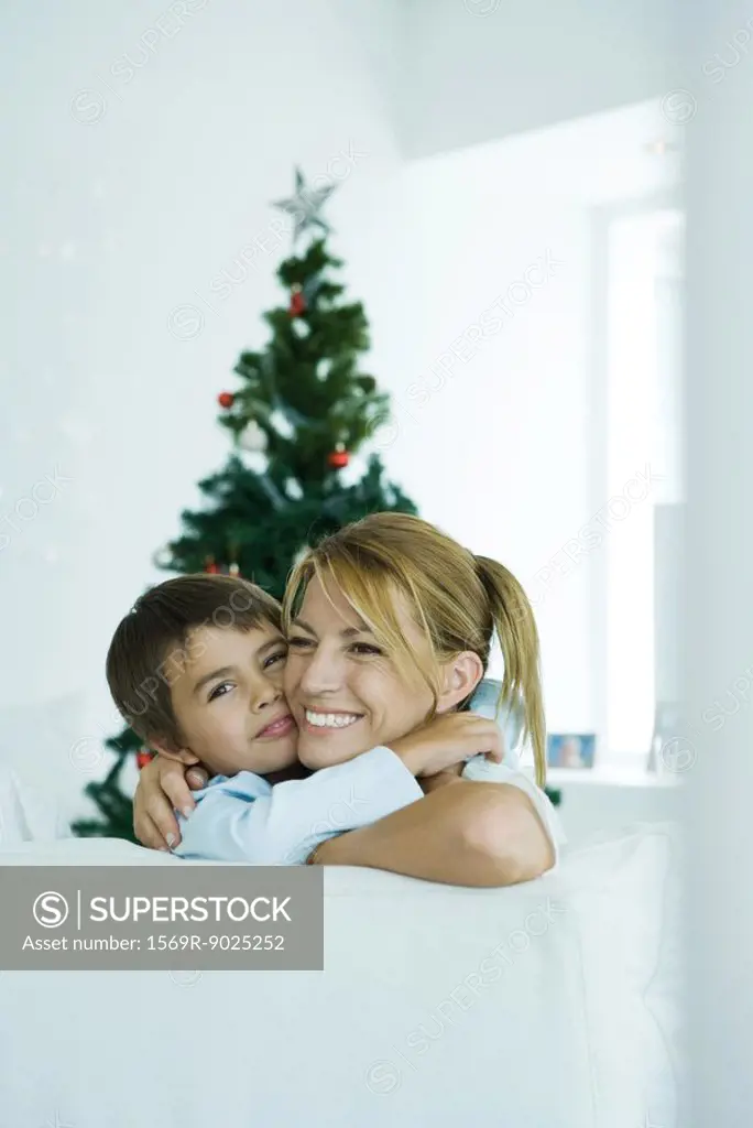 Boy and mother on sofa hugging each other, Christmas tree in background