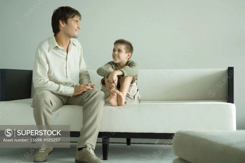 Boy and father sitting on sofa, talking