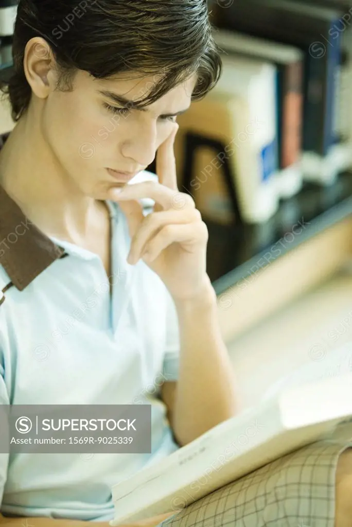 Young man sitting next to shelves of books in library, studying