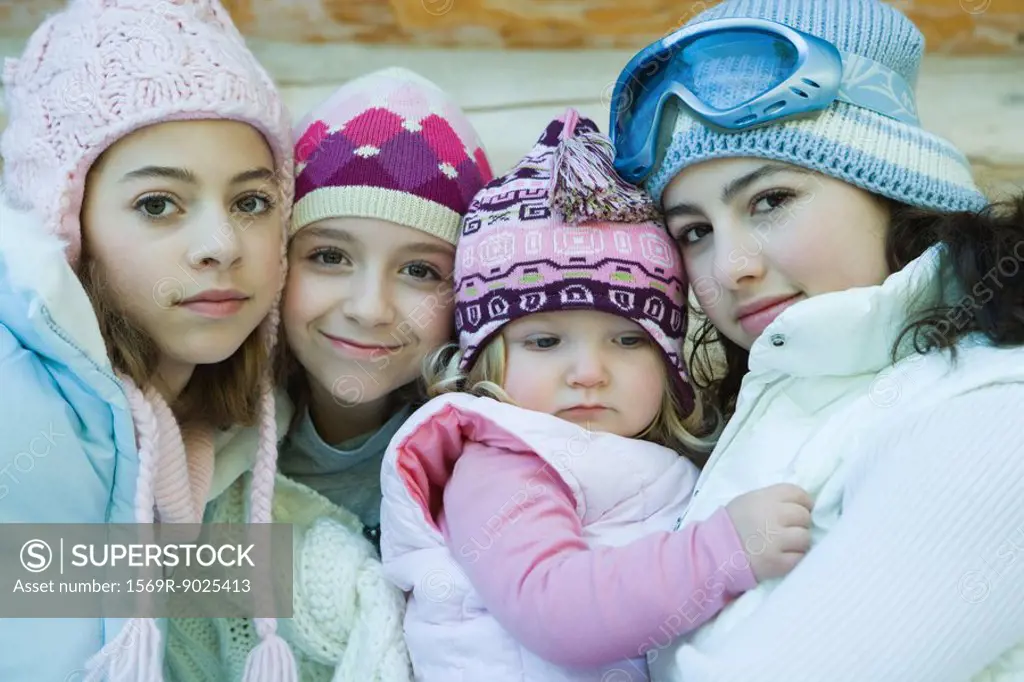 Three teen or preteen girls with toddler, all wearing winter coats and hats, portrait