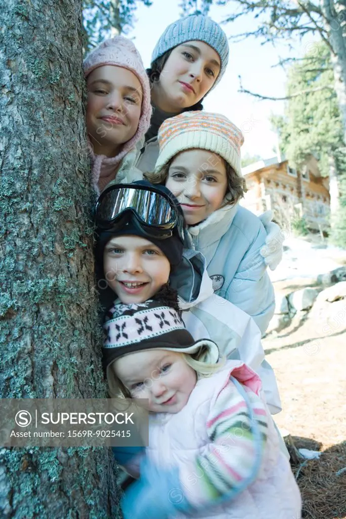Group of teens and children dressed in winter clothes, posing next to tree, portrait