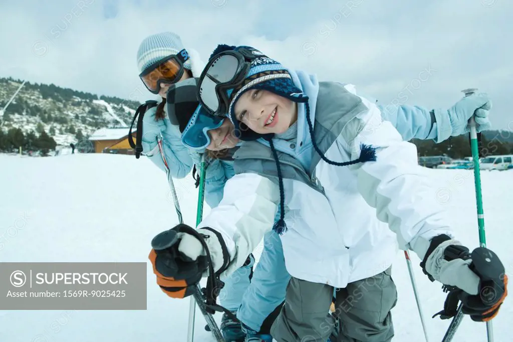 Young skiers on snow, leaning to side and smiling at camera, portrait
