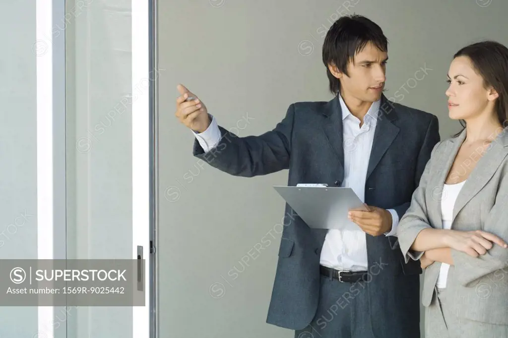 Male real estate agent showing house to female client, standing by sliding glass door, woman looking out, smiling
