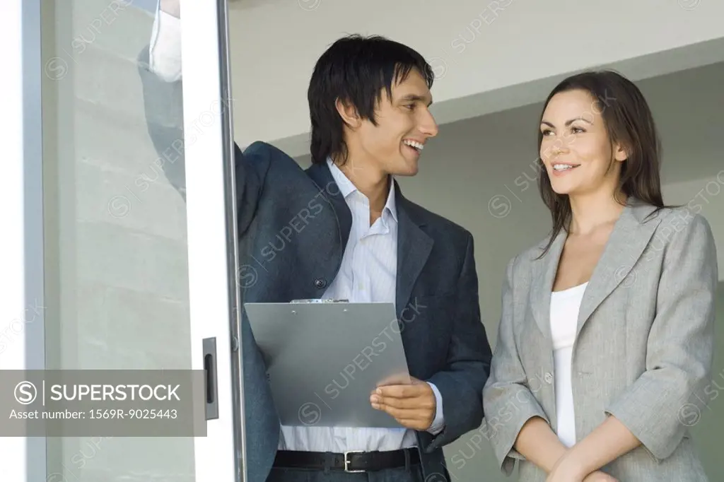 Male real estate agent showing house to female client, standing by sliding glass door, woman looking out, smiling