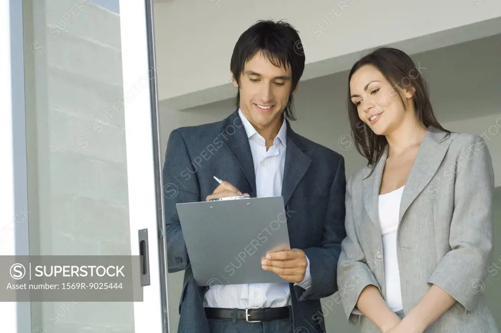 Male real estate agent showing house to female client, writing on clipboard