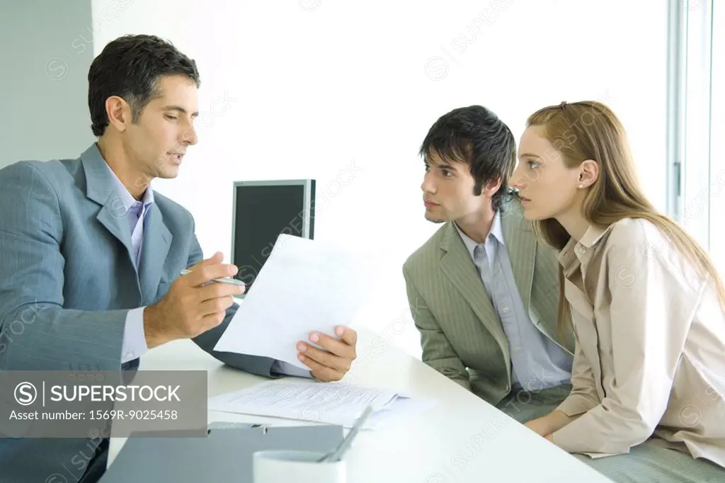 Young couple sitting across desk from businessman, businessman explaining document
