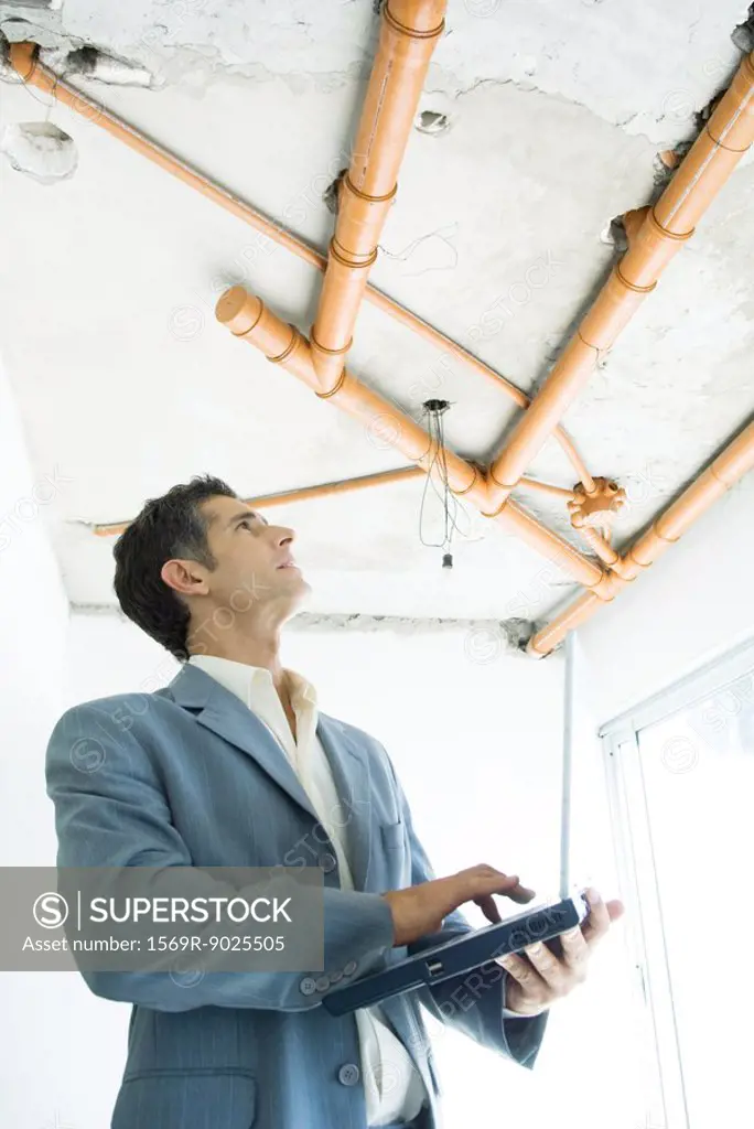 Well-dressed man using laptop, inspecting unfinished home interior