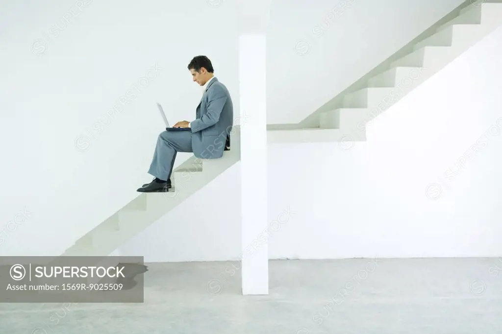 Man in suit sitting on stairs, using laptop
