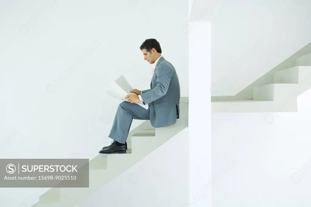 Man in suit sitting on stairs, looking at documents