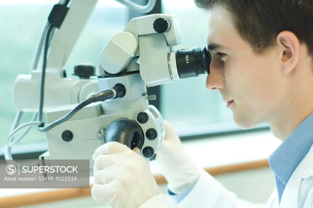 Young male scientist looking through microscope