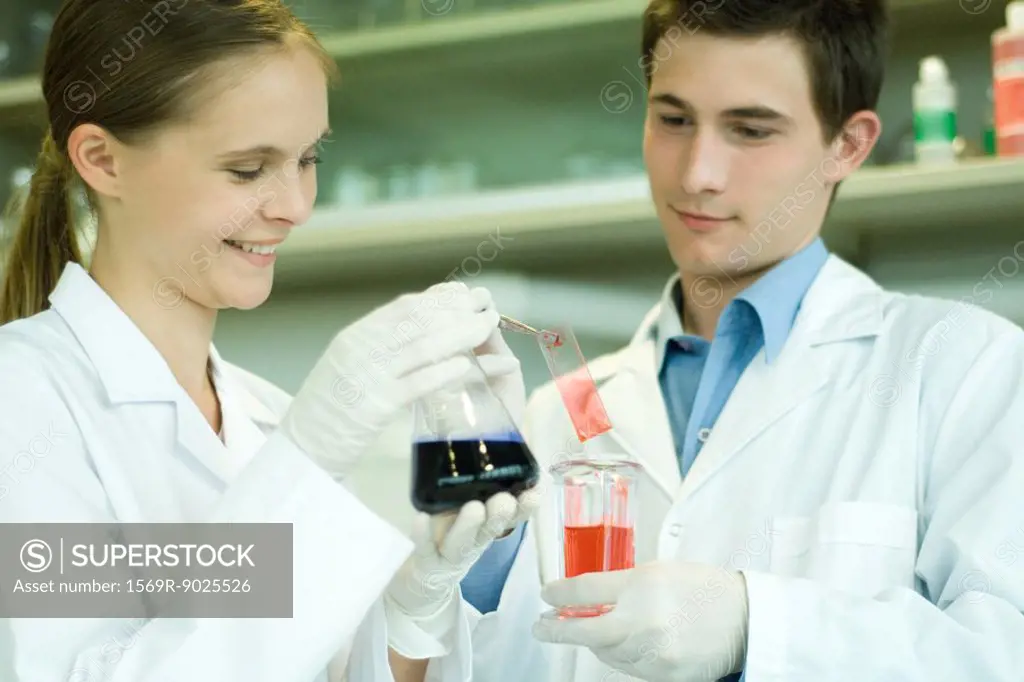 Young male and female scientists holding solutions in lab glassware