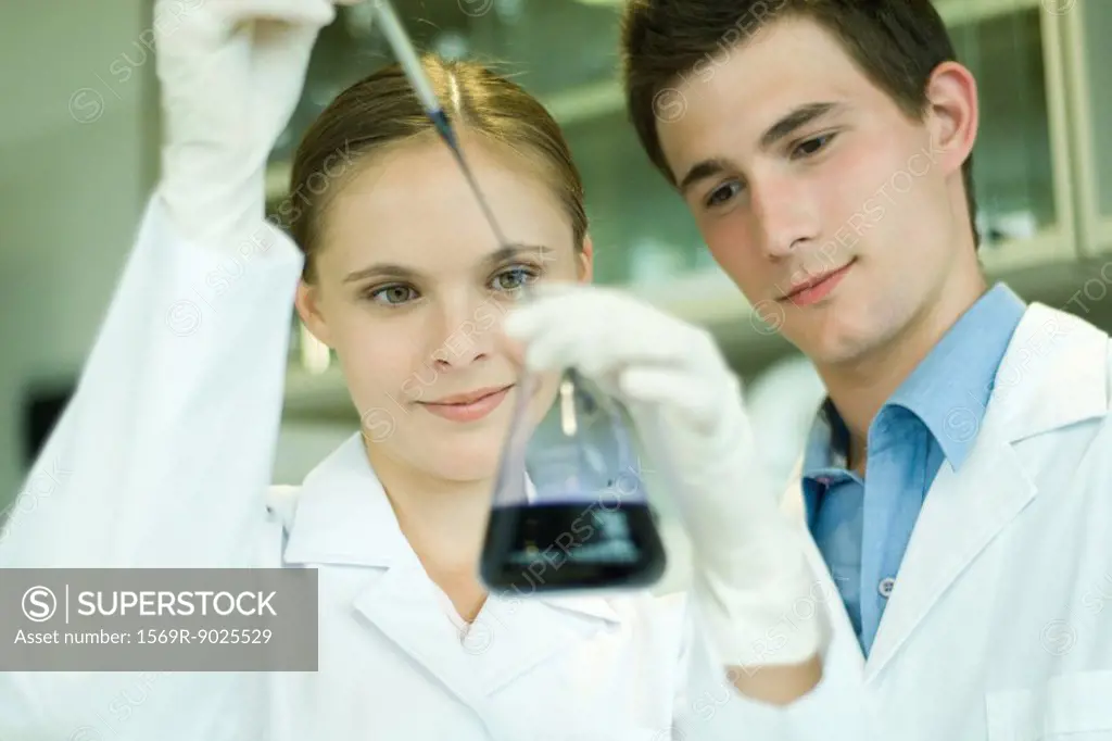 Young male and female scientists, woman holding up dropper and flask