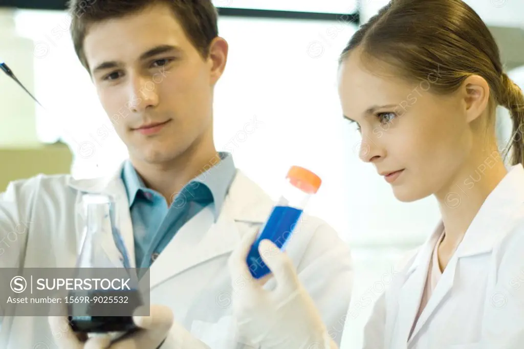 Young male and female scientists holding test tube and flask