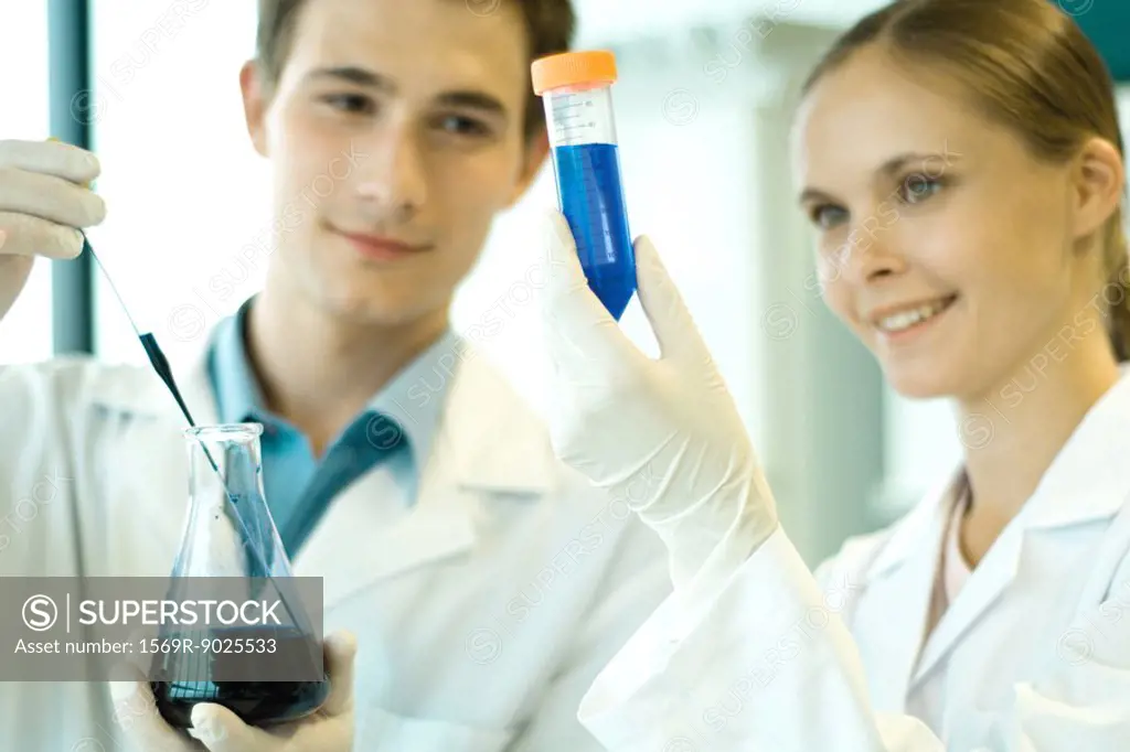 Young male and female scientists holding test tube and flask