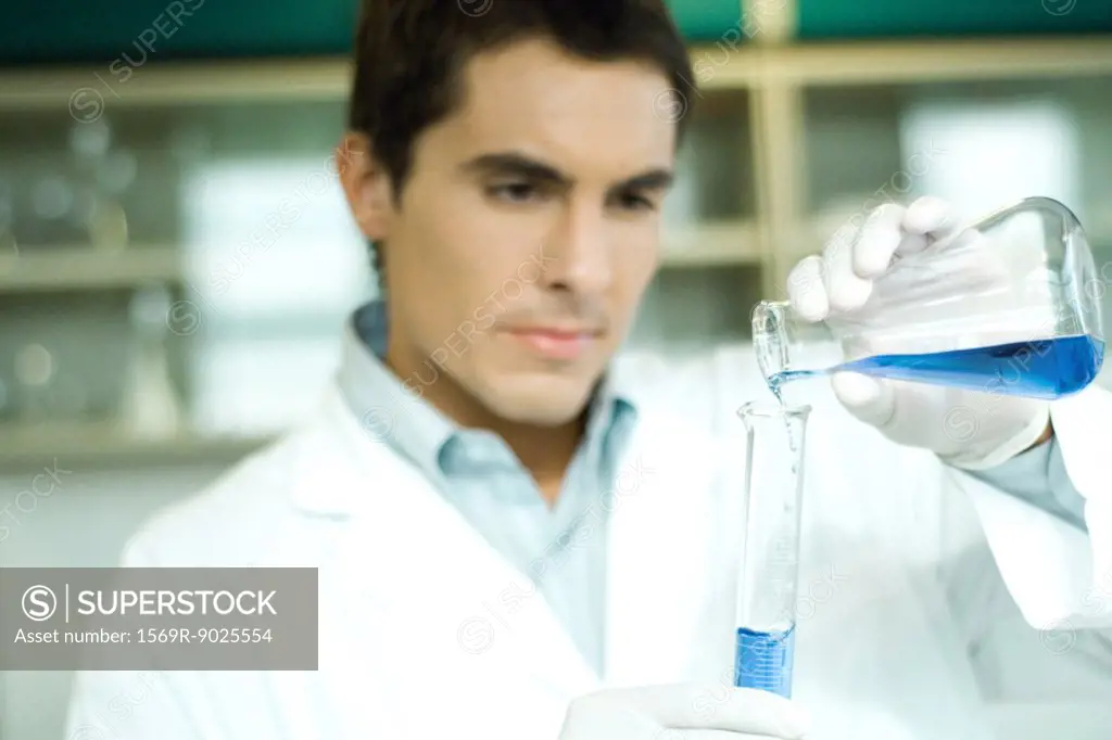 Male lab worker transferring solution from flask to graduated cylinder