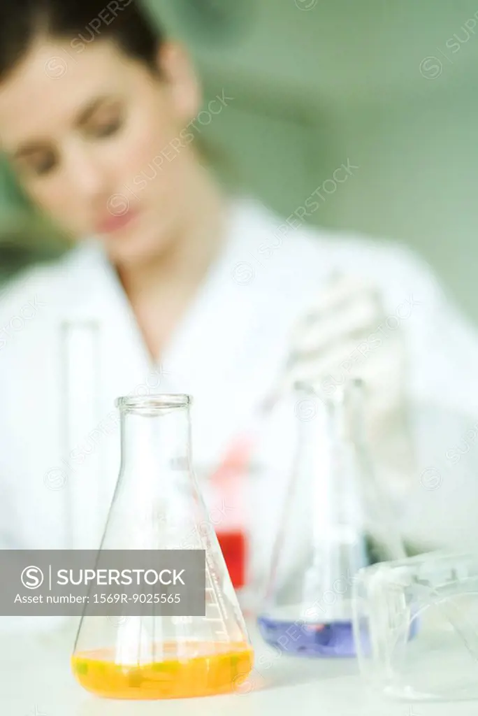 Female scientist working in laboratory, focus on lab glassware in foreground