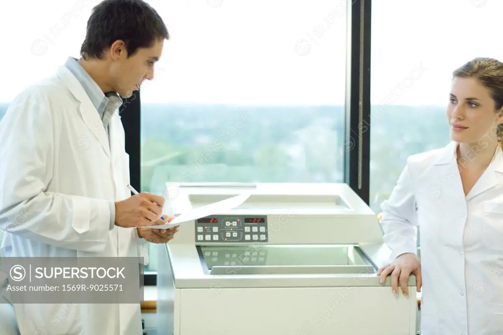 Male and female lab workers standing next to lab machine