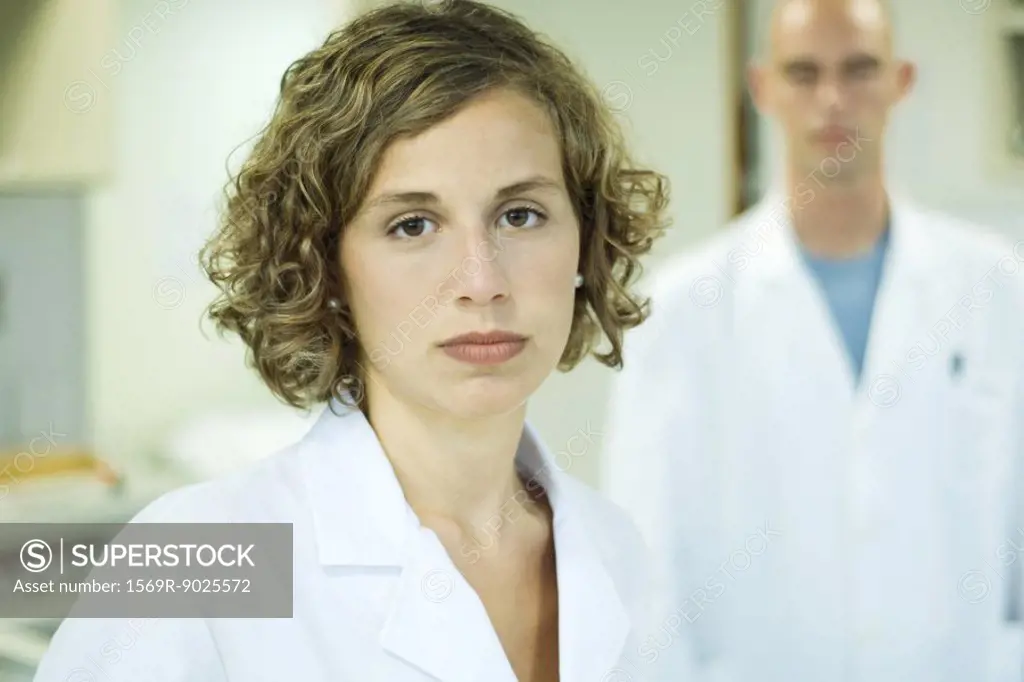 Female doctor looking at camera, male colleague in background, portrait