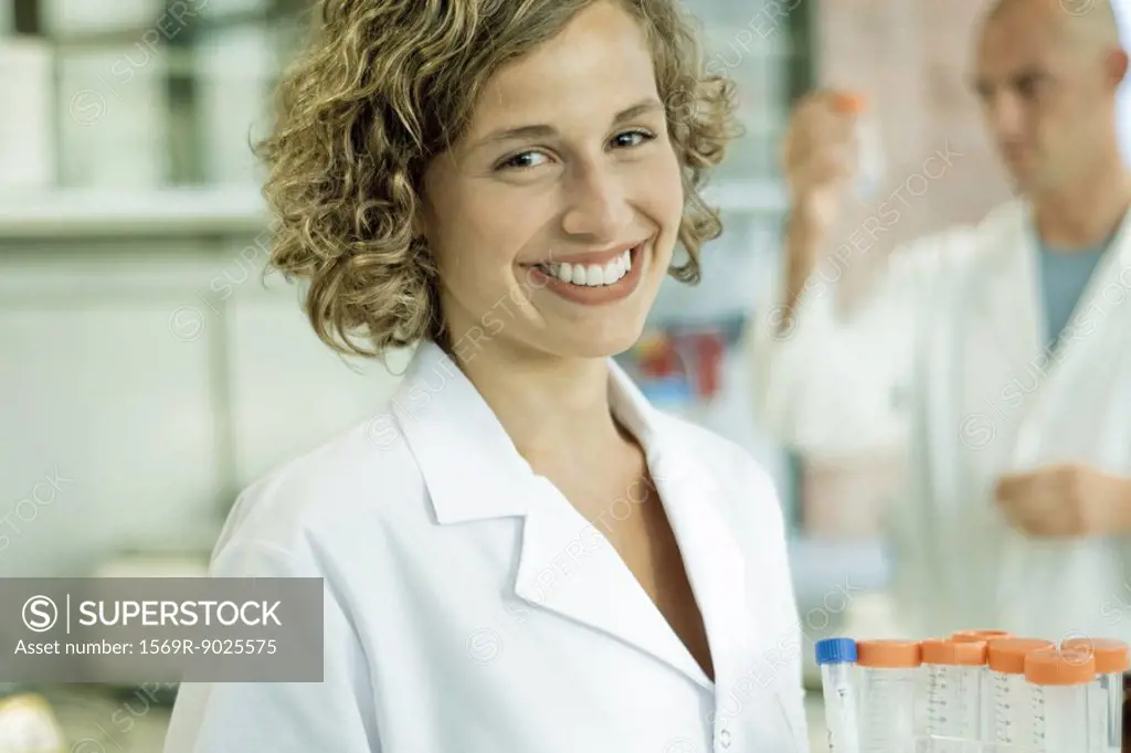 Female lab worker holding rack of empty test tubes, smiling at camera, portrait