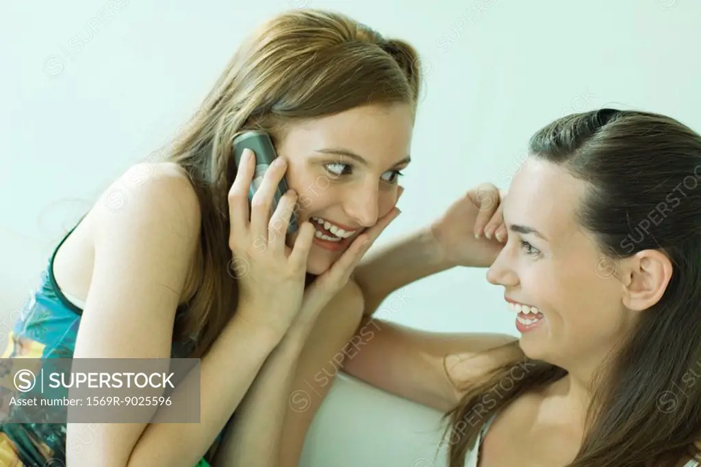 Two young friends smiling at each other, one using cell phone