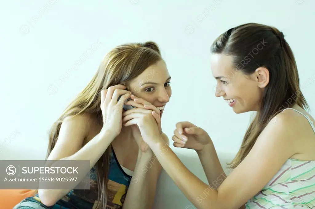 Young woman using cell phone, friend reaching for phone, smiling