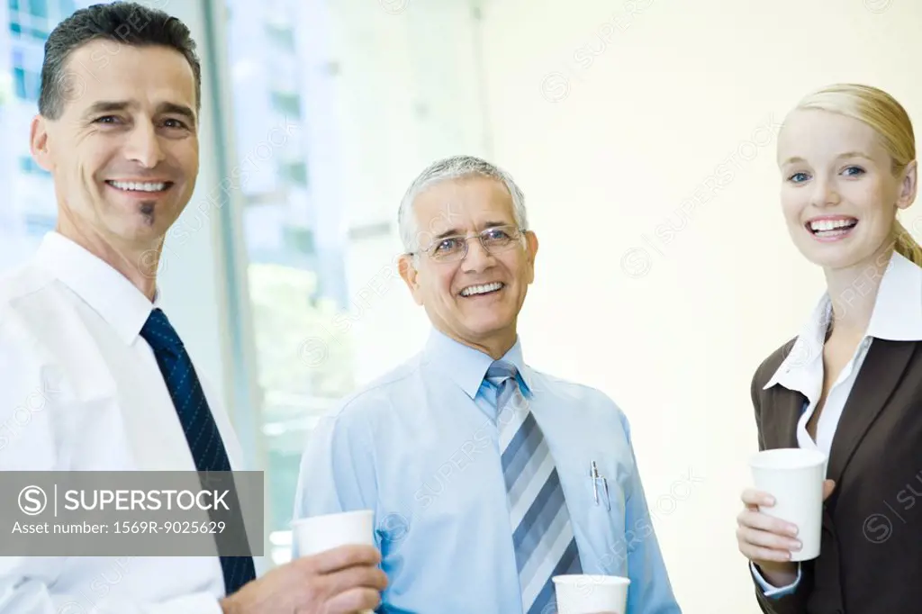 Three business associates smiling at camera, holding hot beverages, portrait