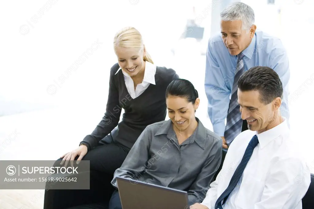 Four business associates looking at laptop computer together, smiling
