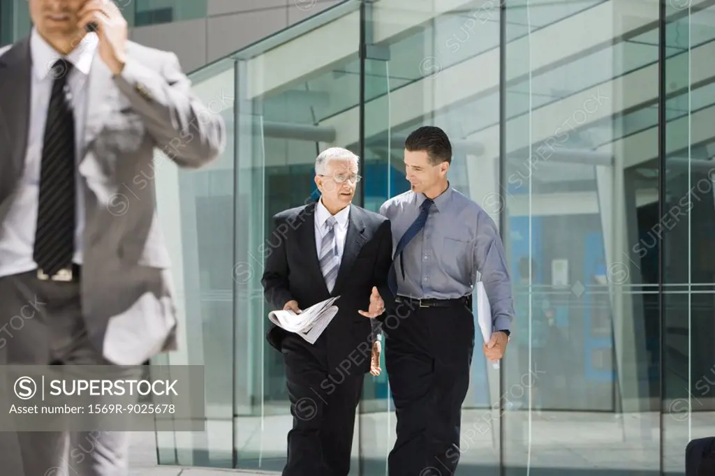 Two businessmen walking together, discussing, building in background