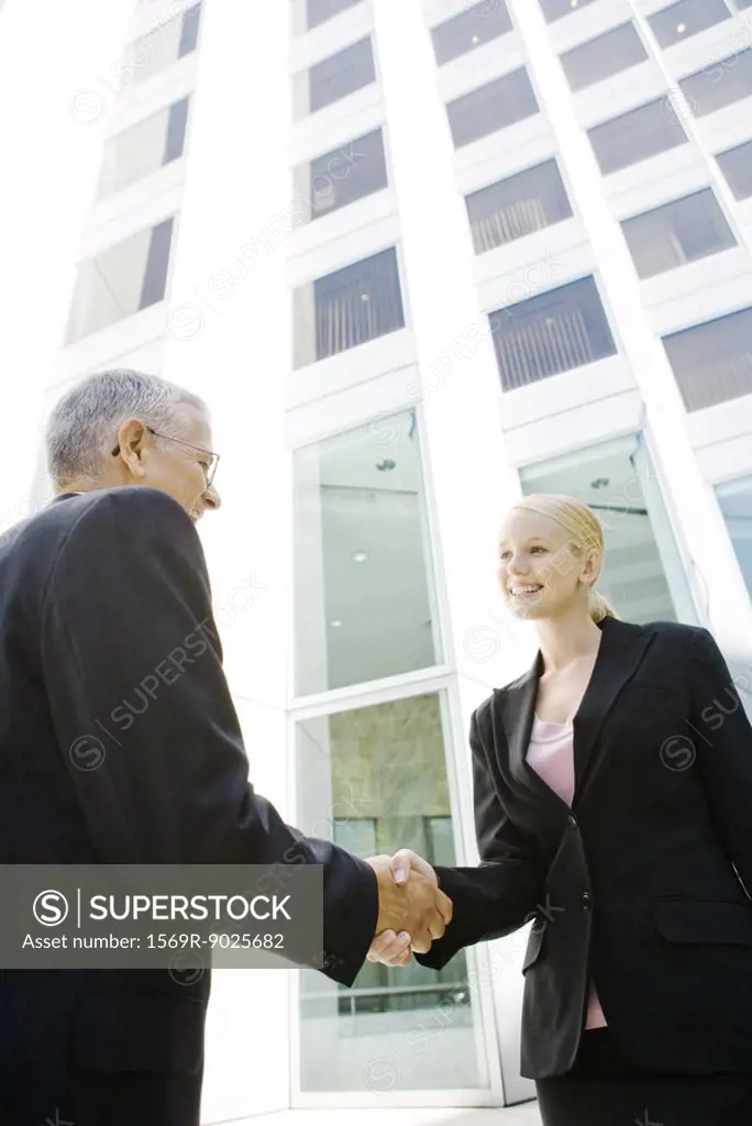 Two business associates shaking hands, smiling, building in background