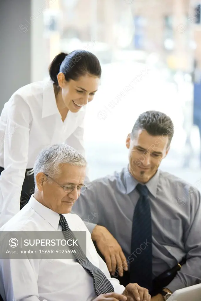 Mature businessman using laptop computer, two colleagues looking over his shoulder