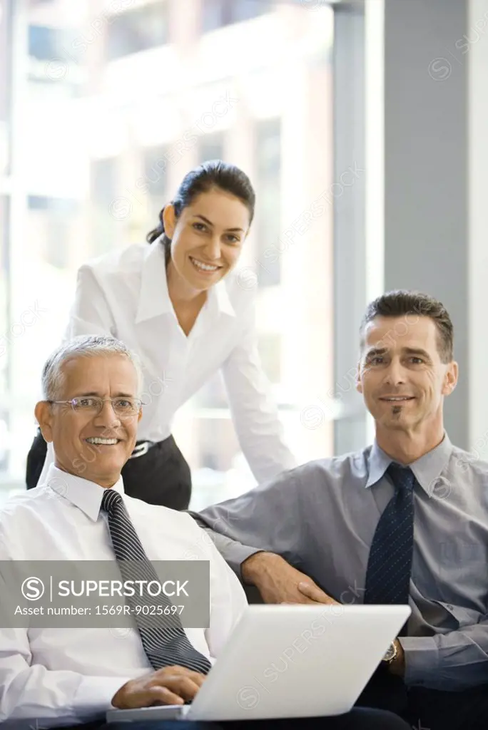 Three business associates smiling at camera, group portrait, one using laptop computer