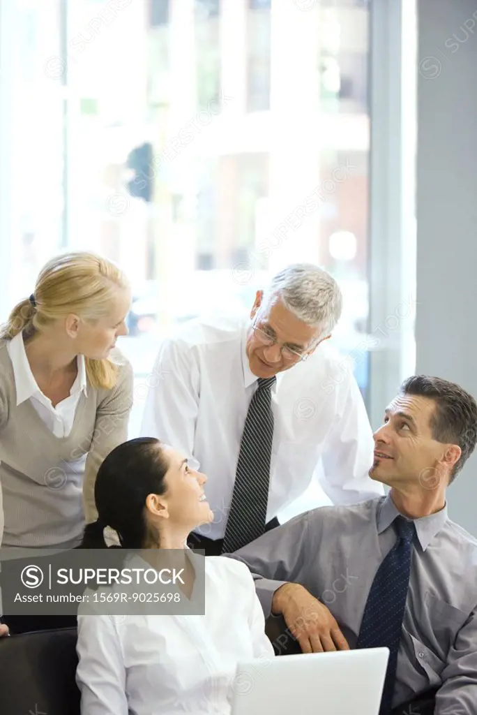 Four business associates smiling at each other, one using laptop computer