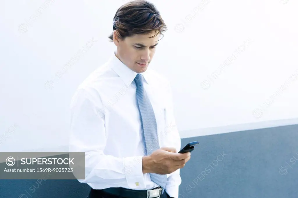 Young businessman looking at cell phone, waist up