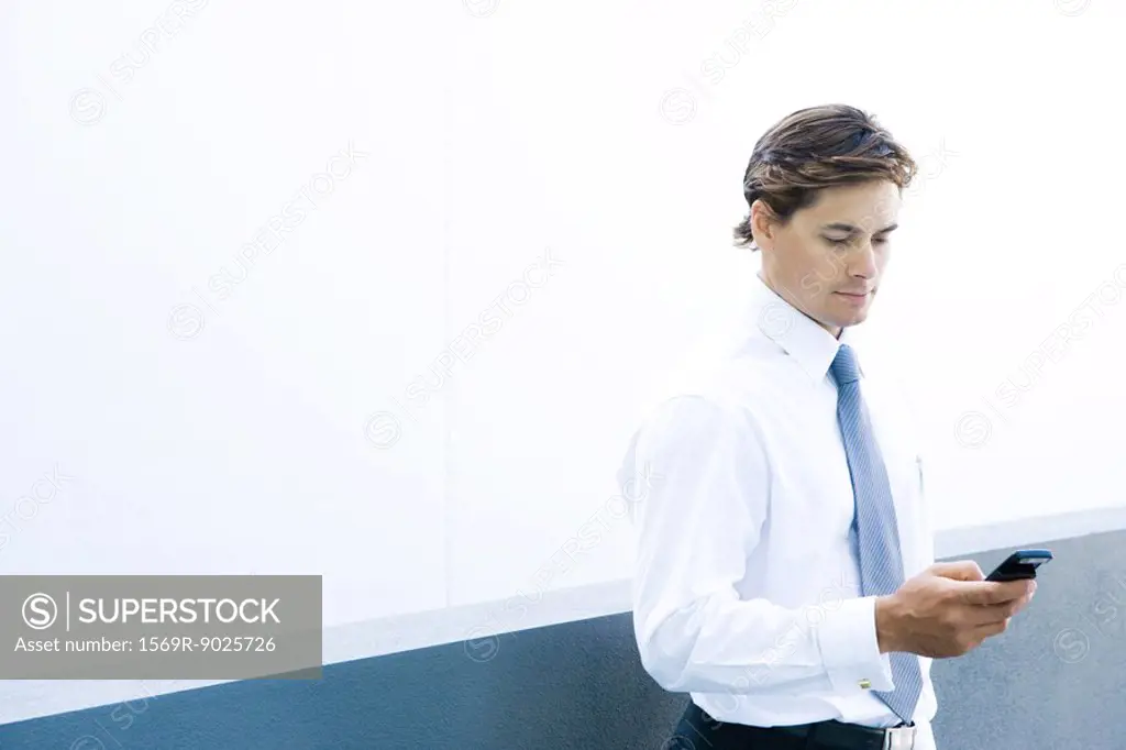 Young businessman looking at cell phone, waist up