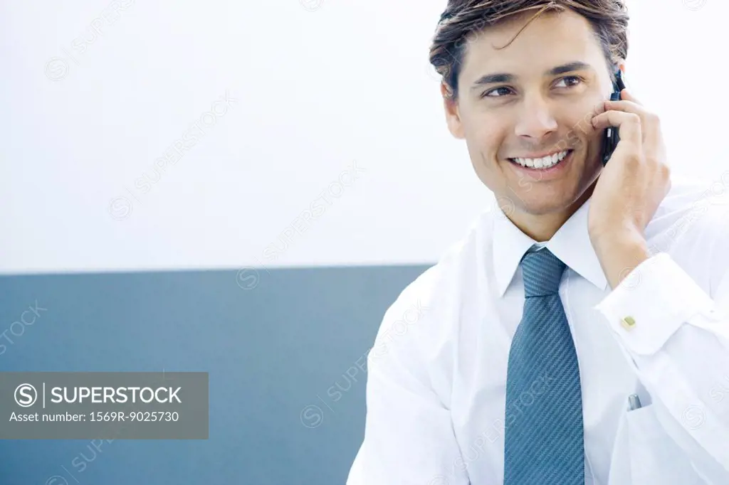 Young businessman using cell phone, smiling, looking away