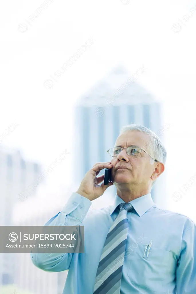 Mature businessman using cell phone outdoors, looking away