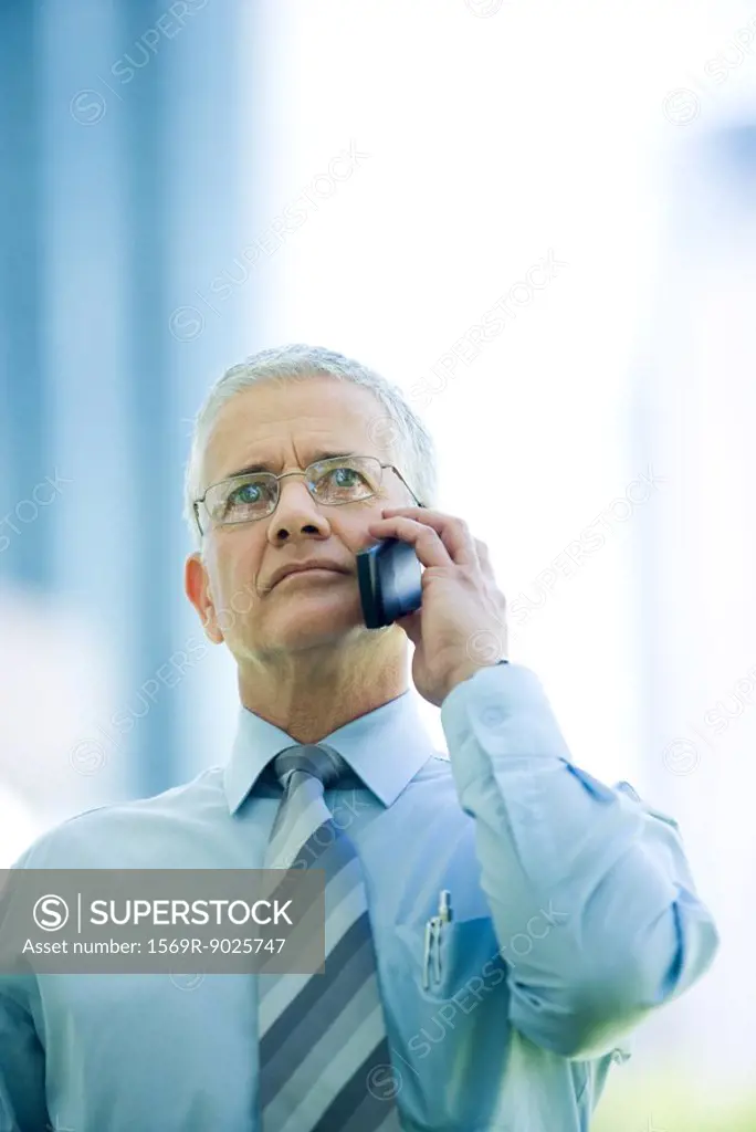 Mature businessman using cell phone, looking up
