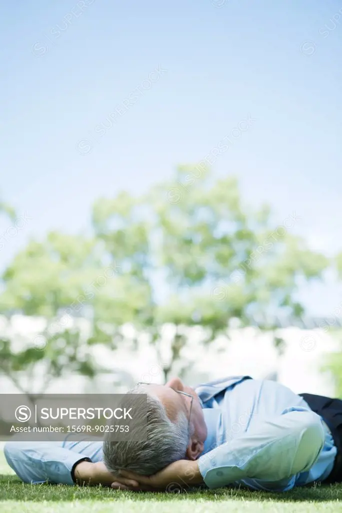 Mature businessman lying on ground outdoors, hands behind head