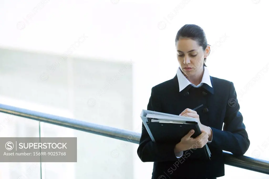Young businesswoman looking at binder, writing, waist up