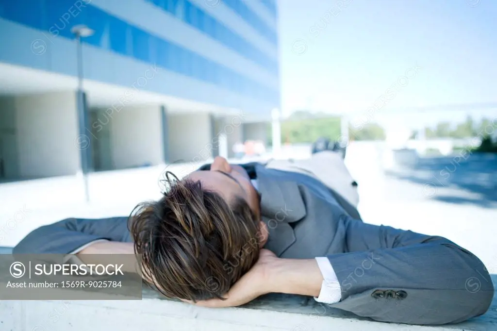 Businessman lying on ground outdoors, hands behind head, full length
