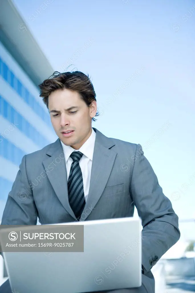 Young businessman outdoors, using laptop computer, looking down