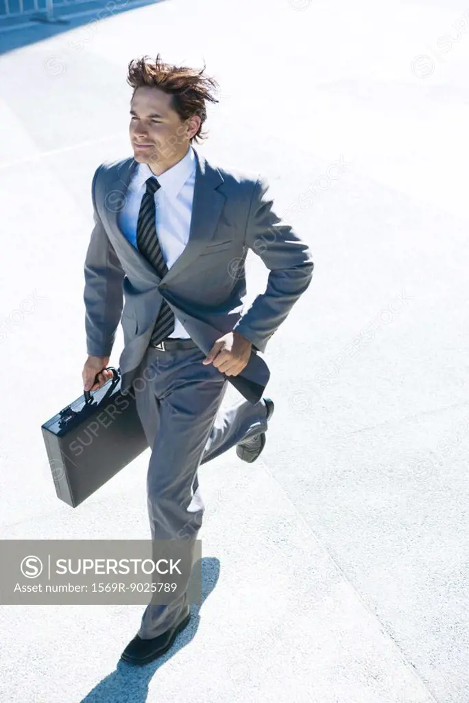 Young businessman running outdoors, carrying briefcase, smiling