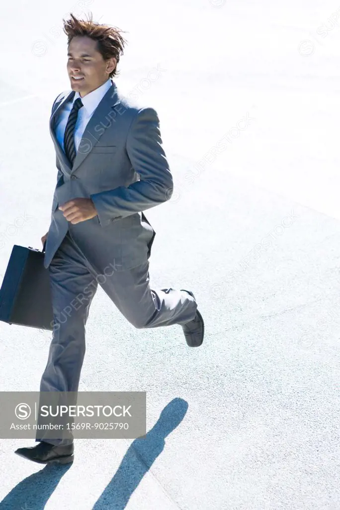 Young businessman running outdoors, carrying briefcase, full length