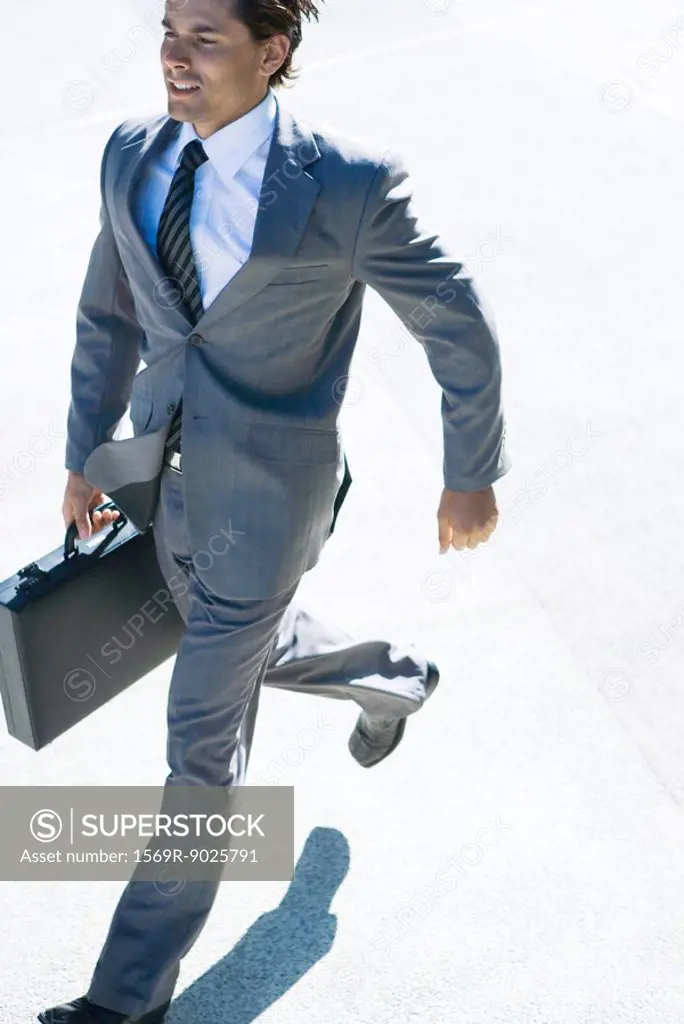 Young businessman running outdoors, carrying briefcase
