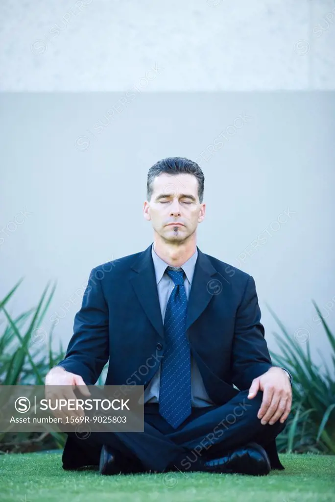 Businessman sitting on ground, meditating, eyes closed, full length portrait