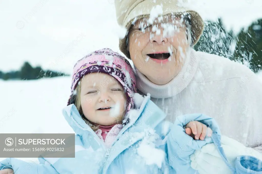 Grandmother and granddaughter in snow, both smiling, eyes closed