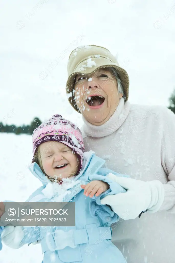 Grandmother and granddaughter being hit with snowballs, smiling