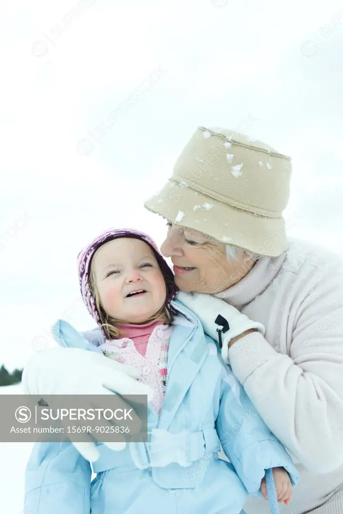 Grandmother embracing toddler in snow, both smiling