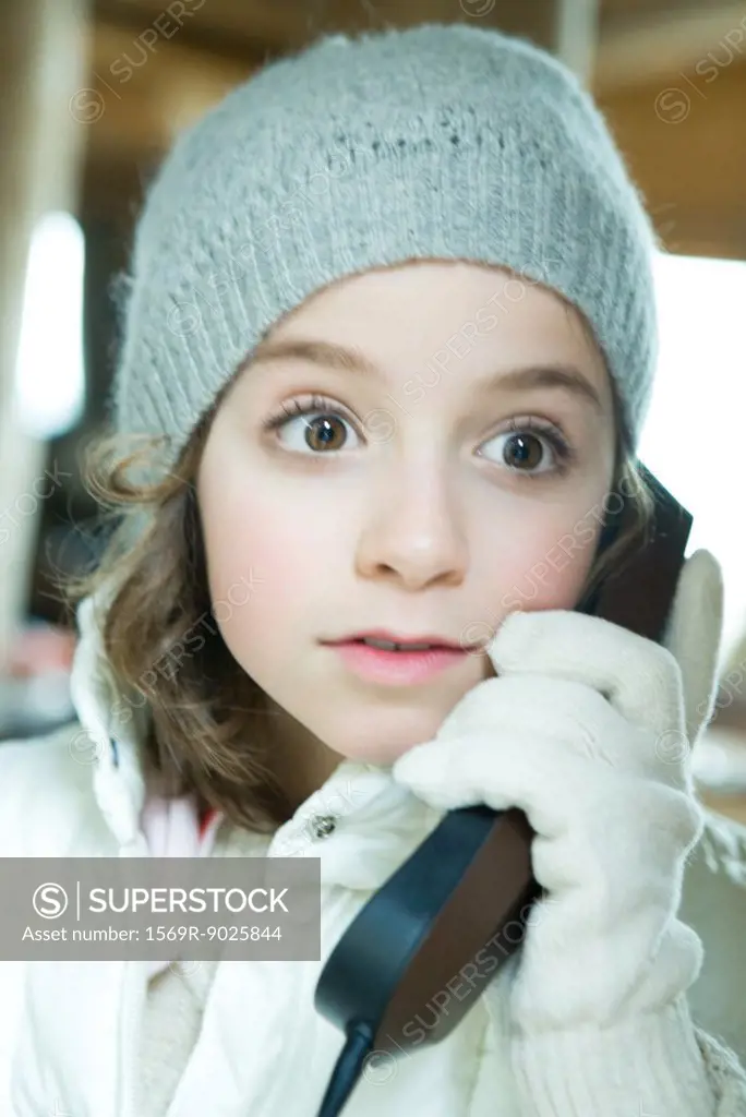 Girl using phone, dressed in winter clothing, looking away with wide eyes